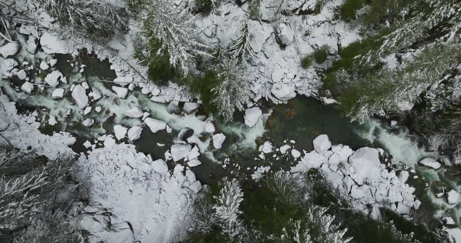 Aerial view of a mountain river flowing through a snow covered forest