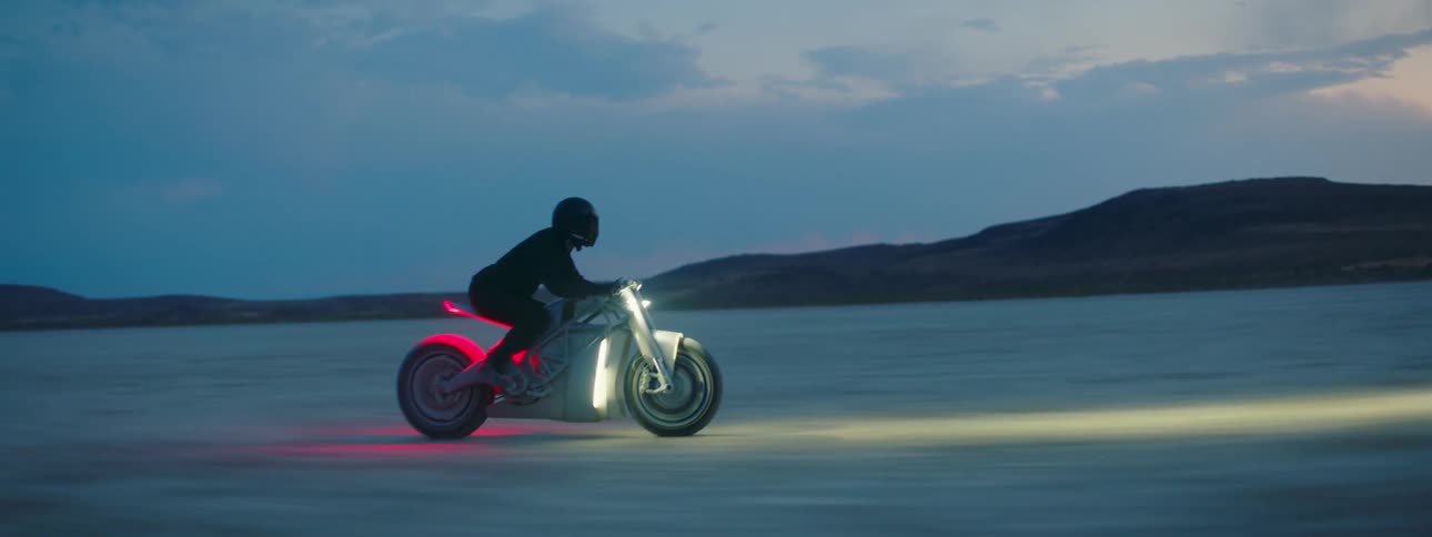 A person riding a motorcycle with bright headlights across a desert landscape
