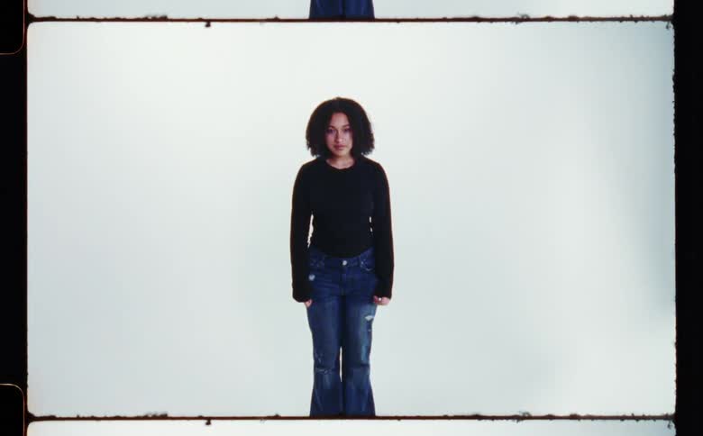 A woman in jeans and a long sleeve tee shirt standing in front of a white background