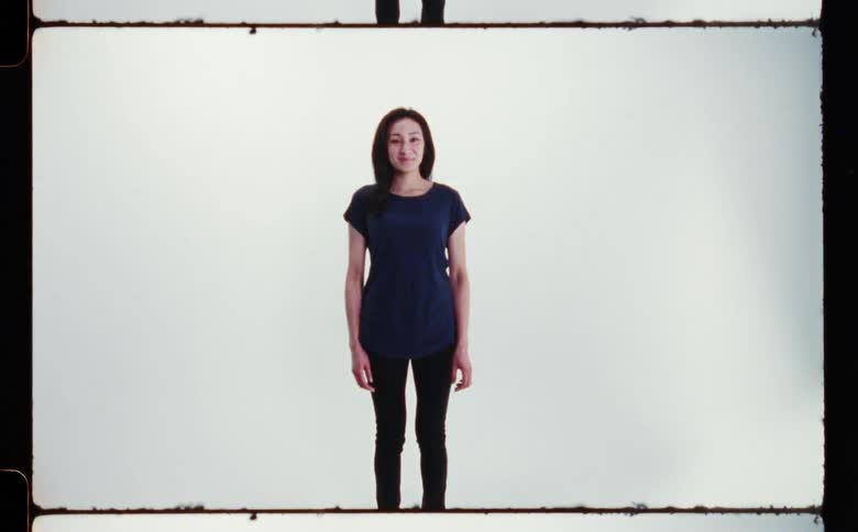 Woman with straight hair dark blue shirt and black pants smiles at camera in photographic studio