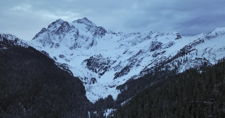 An aerial view of a snowcovered mountain surrounded by steep forested slopes