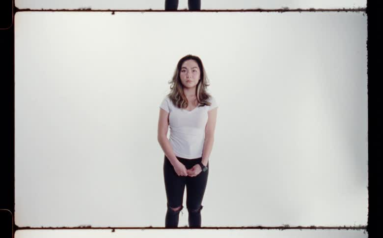 Woman with white shirt and ripped pants poses for the camera in front of white screen backdrop in photography studio