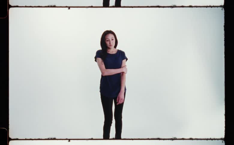 Woman with dark hair purple blouse and black pants poses for the camera in the studio touching her arm