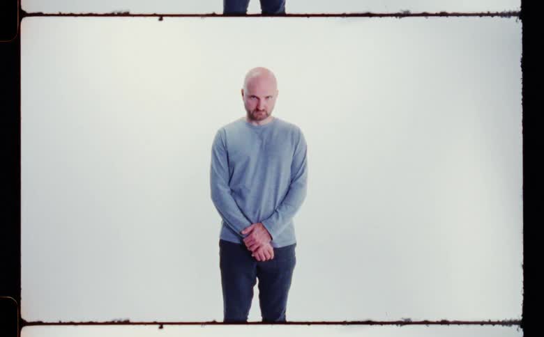 A bald man with a beard standing in front of a white background