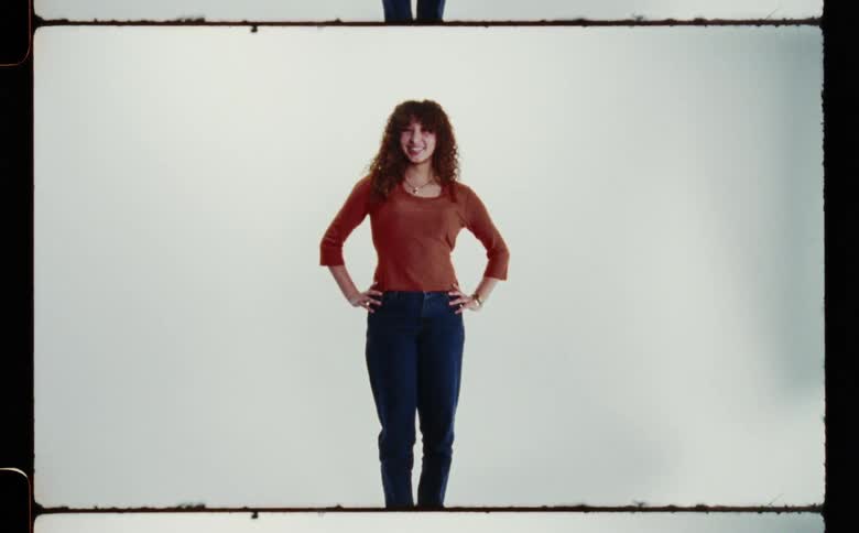 Woman with curly hair red shirt and jeans poses for the camera in the studio