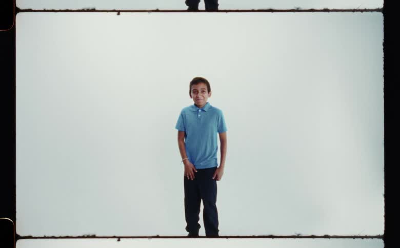 Youth smilesand laughs while posing against pale background