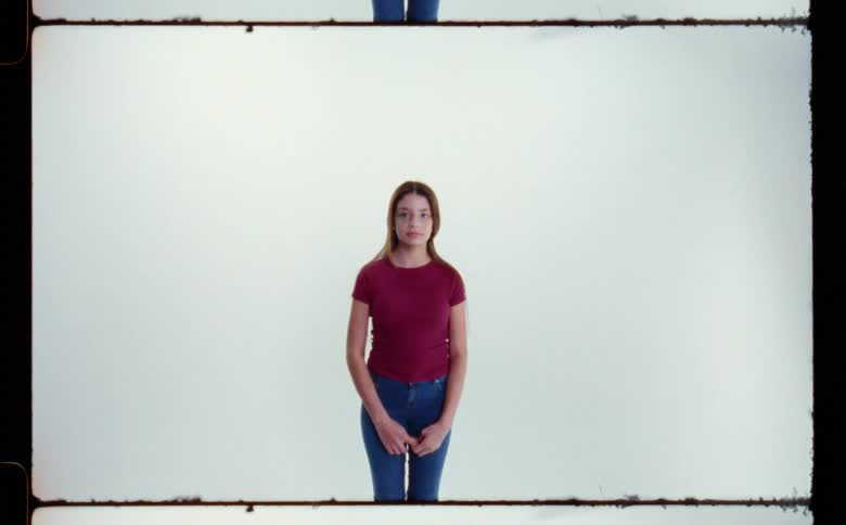 A teenage girl in a red tshirt and jeans standing with her hands in front of her against a white backdrop