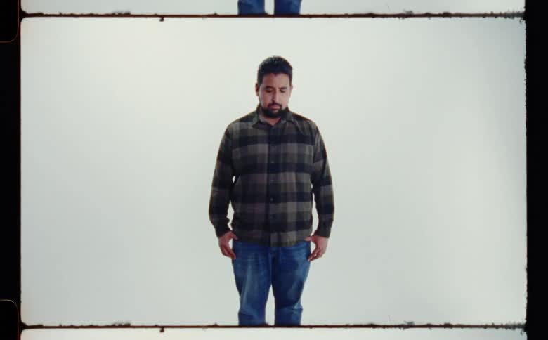 Man with beard and green plaid shirt and jeans poses for the camera in the studio