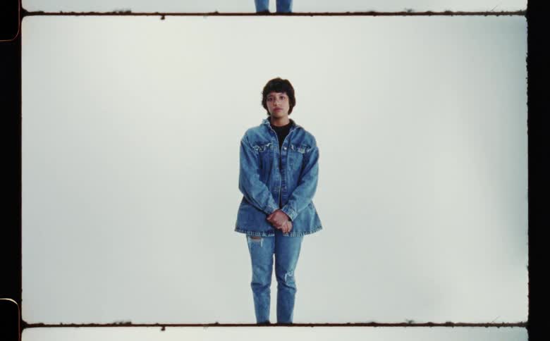 Woman with denim jacket and ripped jeans poses for the camera in the studio