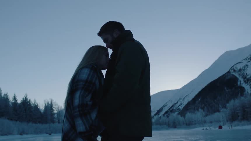 A man and woman kiss on a lake