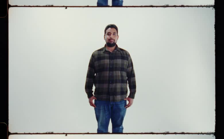 Man with beard dark green plaid shirt and jeans poses for the camera in front of white screen backdrop in photography studio