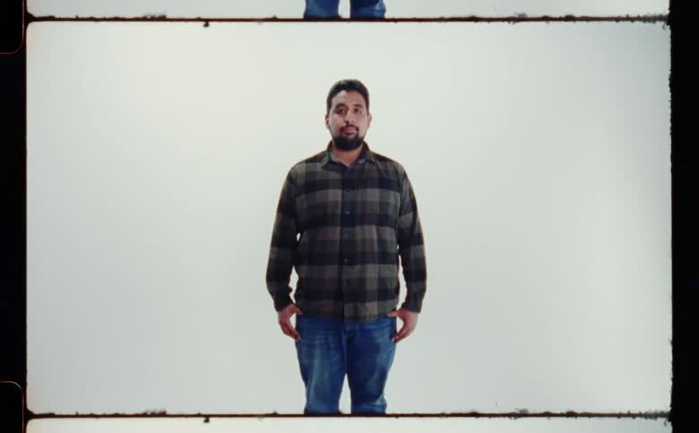 Woman with beard green plaid shirt and jeans poses for camera in front of white screen backdrop in photography studio