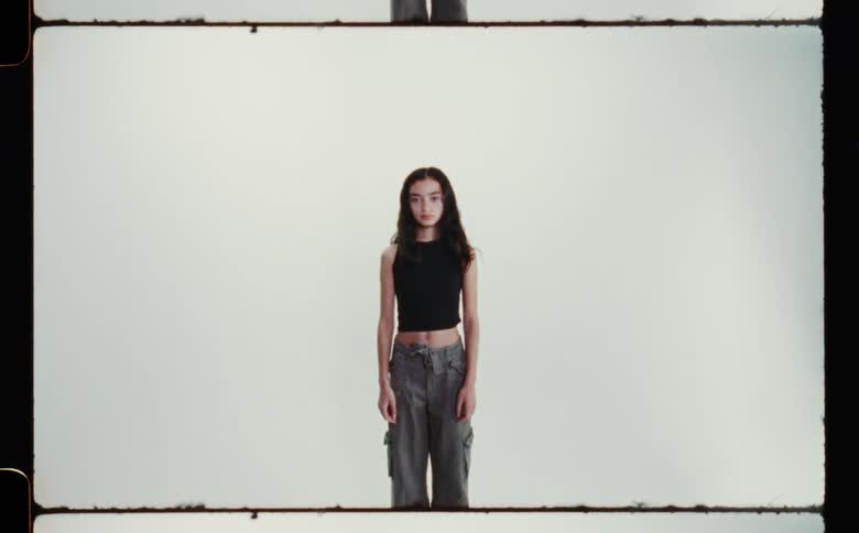 A teen girl wearing a cropped tank top in front of a white background