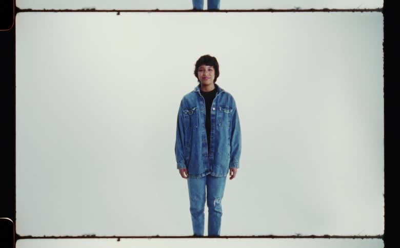 Woman with denim jacket and ripped jeans poses for the camera in the studio smiling