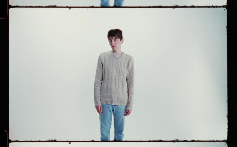An androgynous model glances up at the camera nervously while standing in front of a blank screen