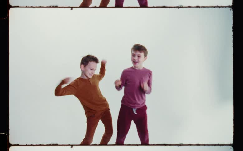 Two boys smile while dancing against a white and blue background
