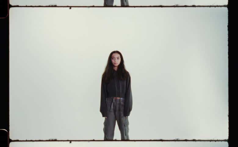A teenage girl wearing a black sweatshirt and grey pants standing with her arms at her sides against a white backdrop