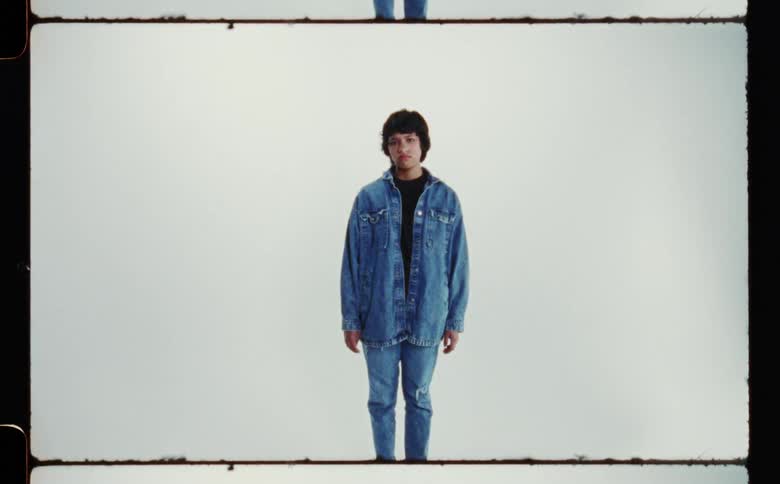 Woman with denim jacket and jeans poses for the camera in front of white screen backdrop in photography studio