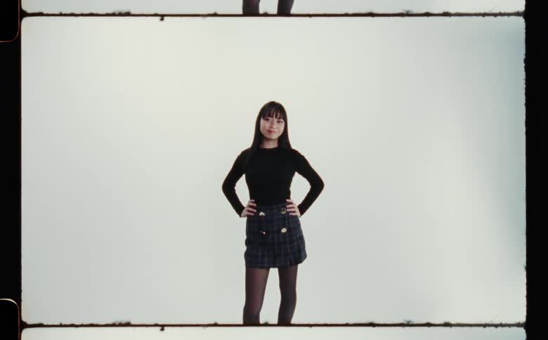 A woman wearing a black long sleeve and black skirt standing with arms on her hips in front of a white backdrop