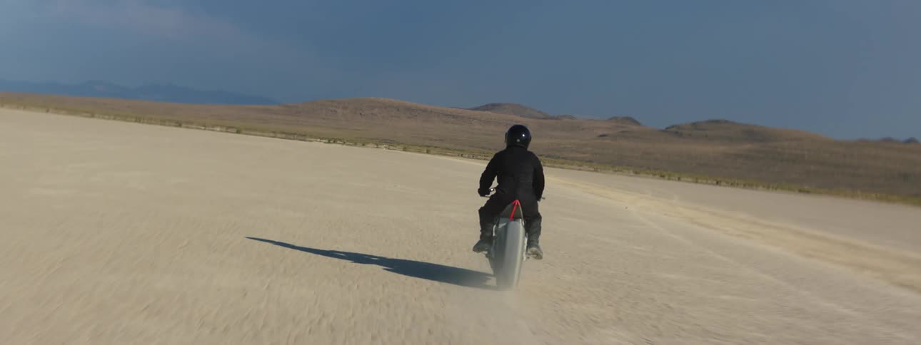 Upside down then normal shot from behind of a person riding a motorcycle in the desert during a sunny day
