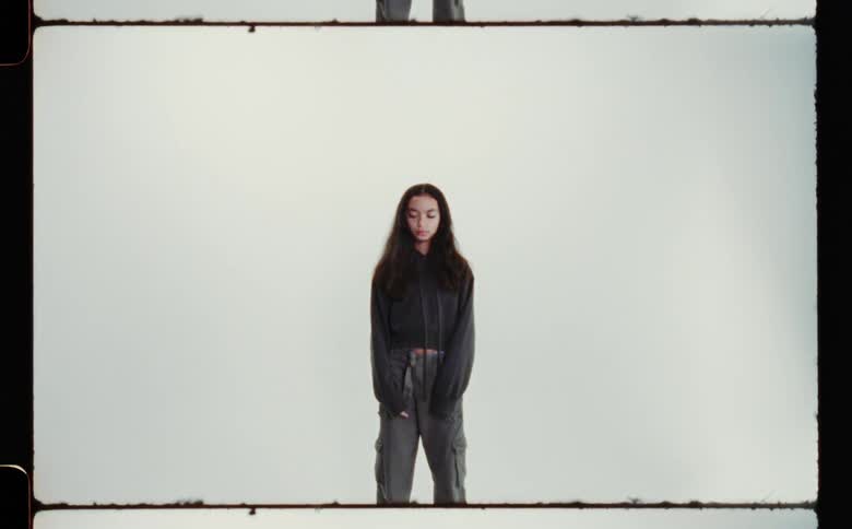 Girl with black shirt and gray pants poses for the camera in front of white screen backdrop in photography studio