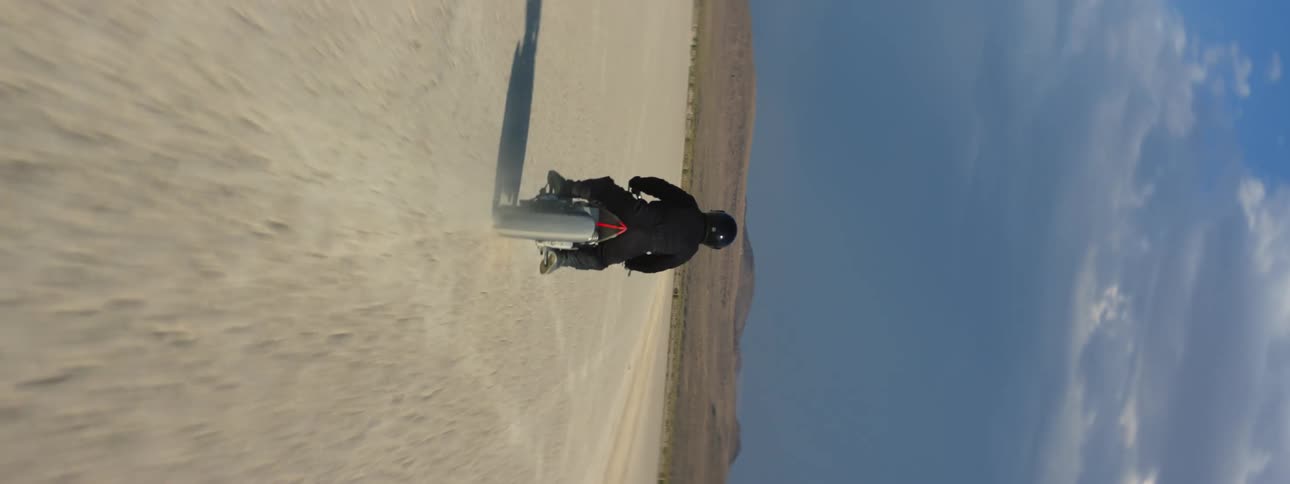 A rider dressed in black traveling in the desert on a motorcycle under a blue sky