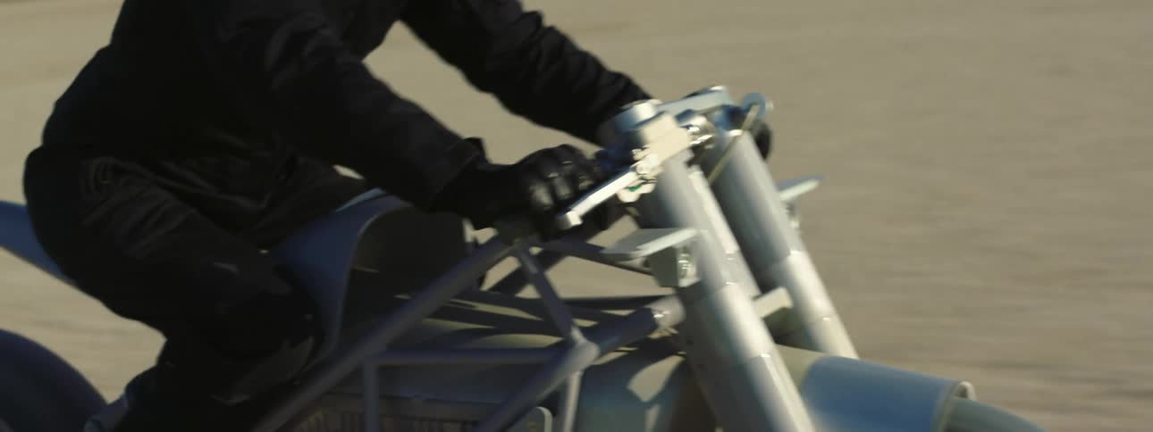 Biker wearing dark clothing rides silver motorcycle across the desert