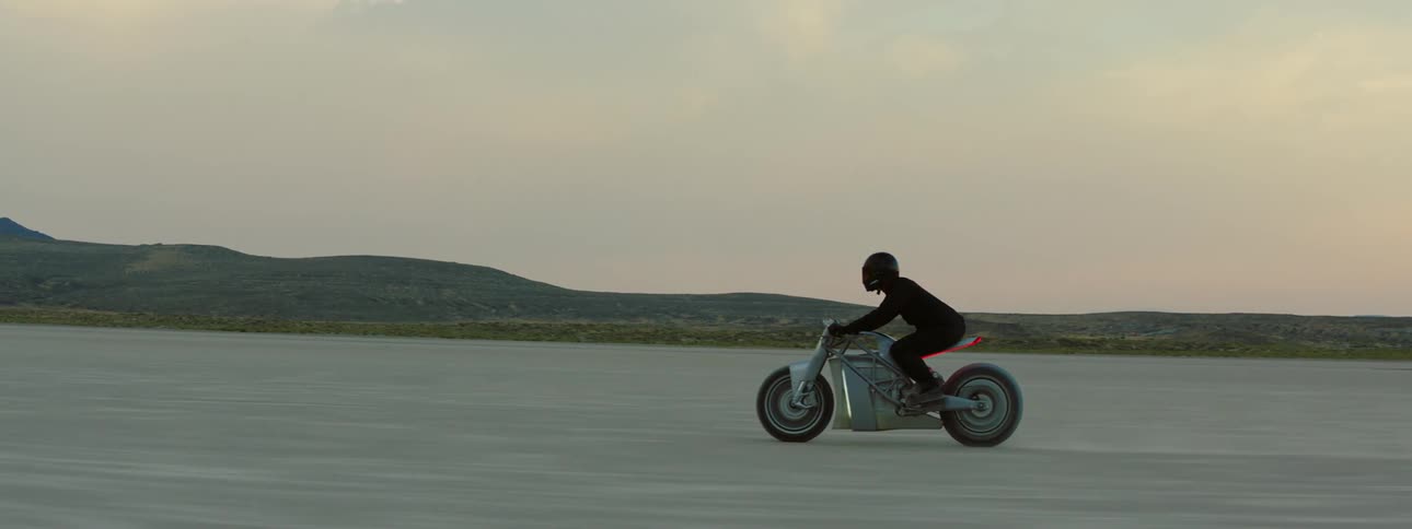 A man is riding a motorcycle through the desert at dusk