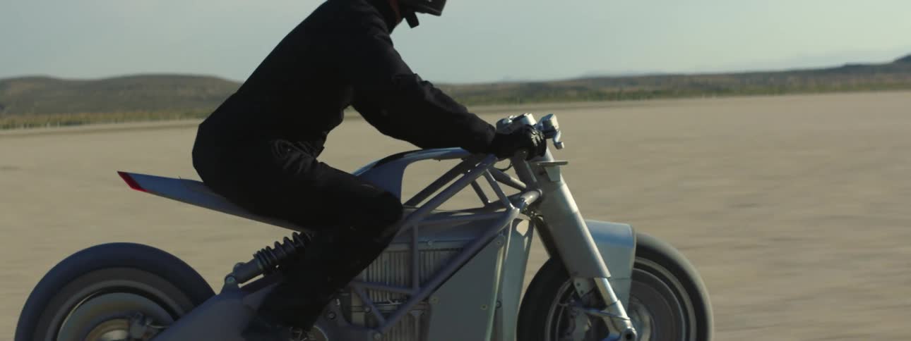 Person riding at high speed on motorcycle through desert landscape with mountains in the background
