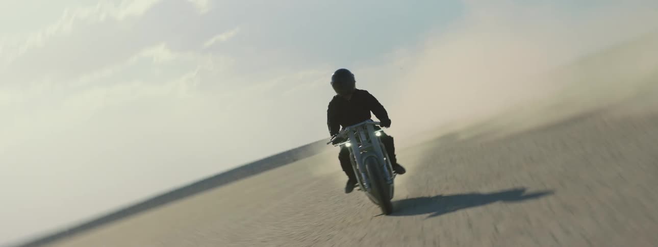 Motorcyclist rides across arid plain kicking up dust