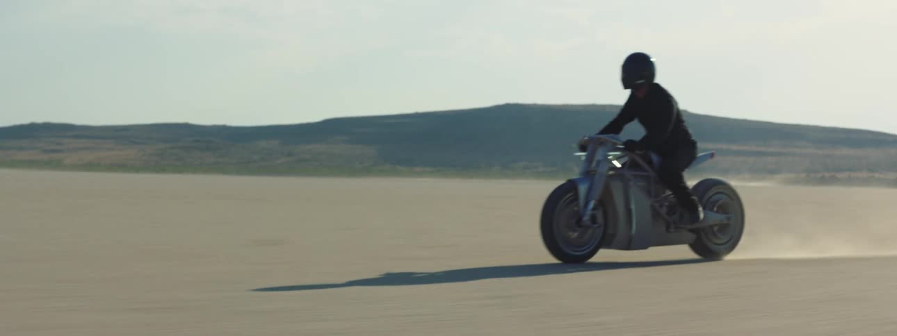 Motorcyclist rides motorcycle across arid plain near mountains