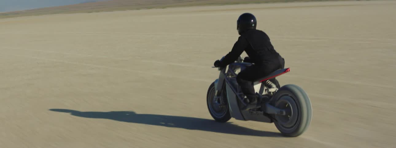 A motorcycle travels across the desert as the rider is wearing a black jacket and helmet