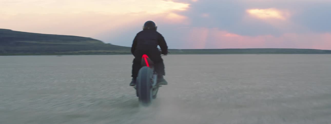 Person wearing a helmet is riding a motorcycle through the desert flats at dusk