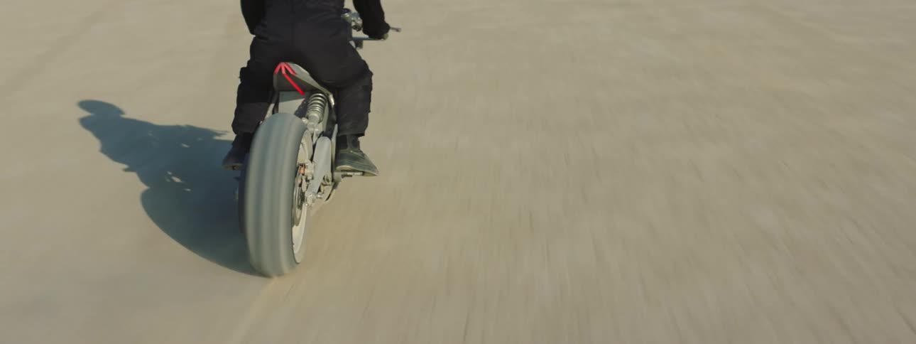 Person wearing a helmet riding on a motorbike through the desert flatland on a sunny day