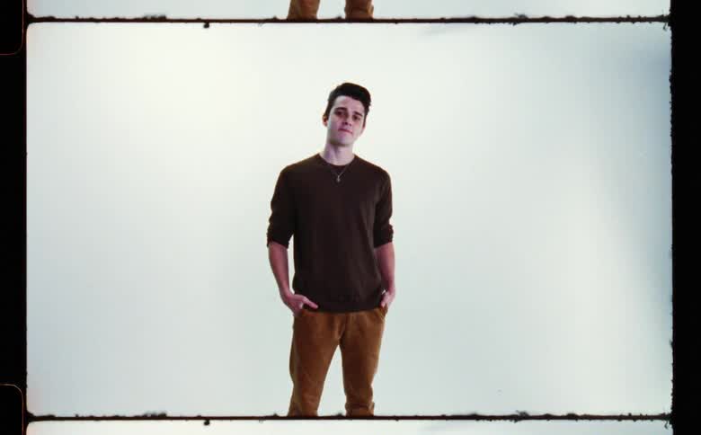 Man with brown sweater and pants poses for the camera in front of white screen backdrop in photography studio
