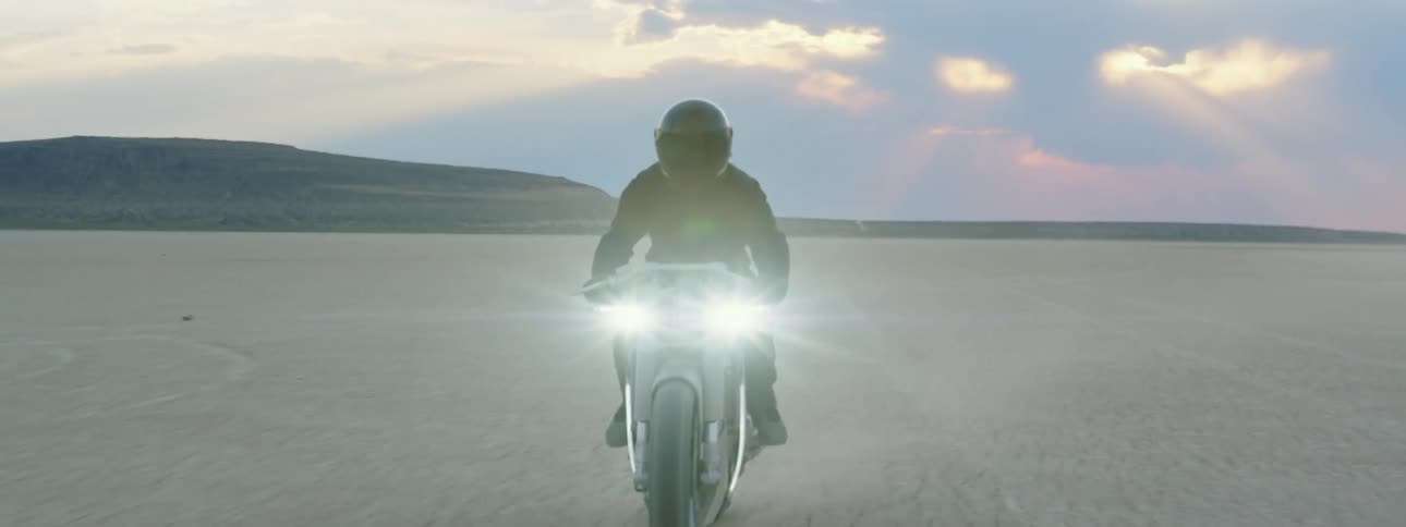 Person on motorcycle with headlights on riding through the desert midday