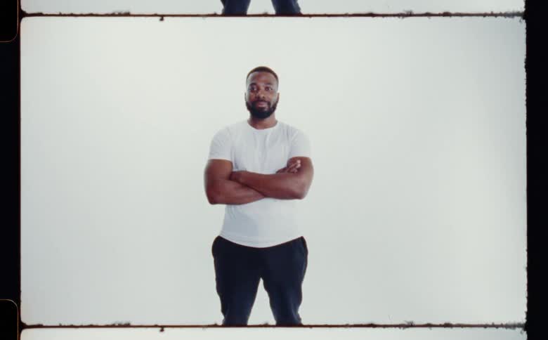 Black man standing with arms crossed wearing white shirt and black pants