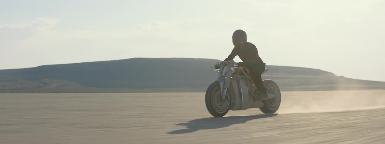 Motorcyclist rides motorcycle across desert kicking up dust