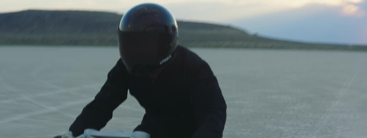 Man with black helmet and jacket rides motorcycle at sunset in the desert