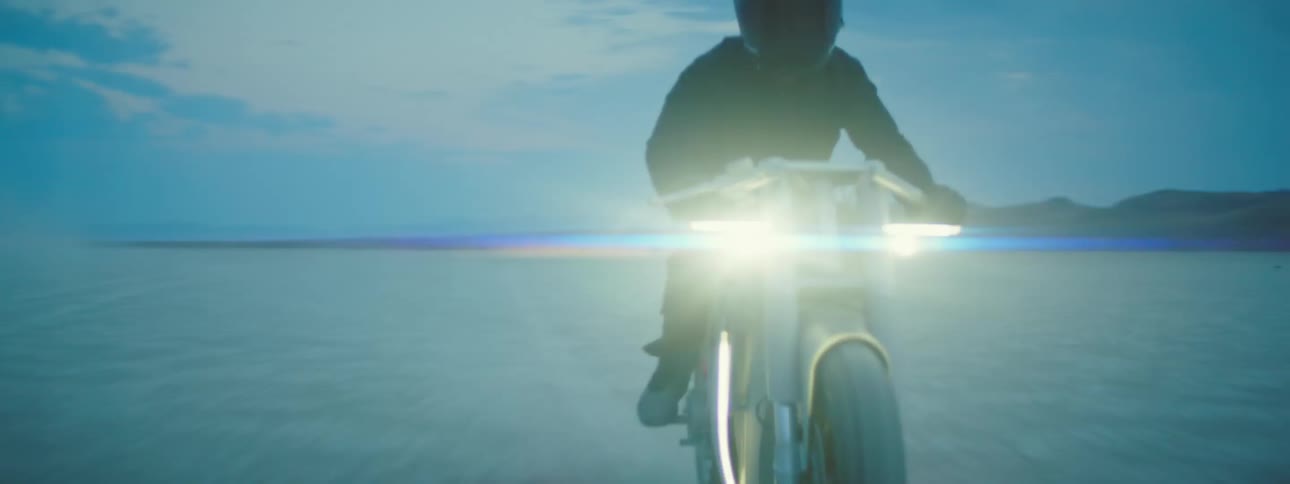 A person riding a motorcycle across a desert landscape at sunrise