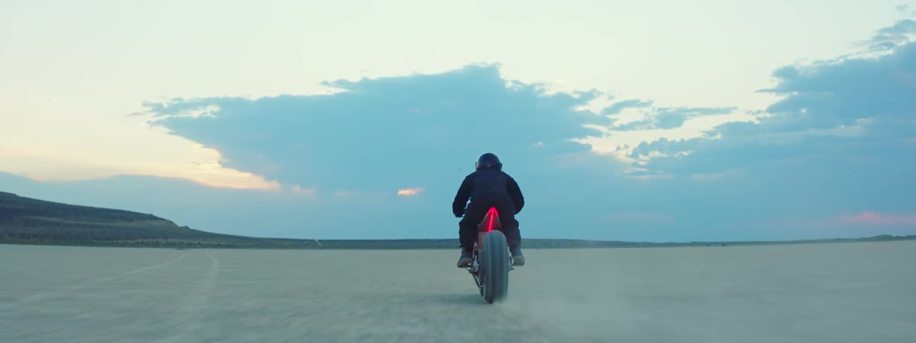 A man is driving a motorcycle through the desert at dusk