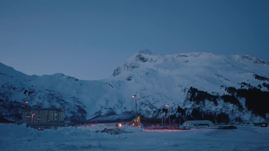 A group of buildings nestled at the foot of some snow-covered mountains