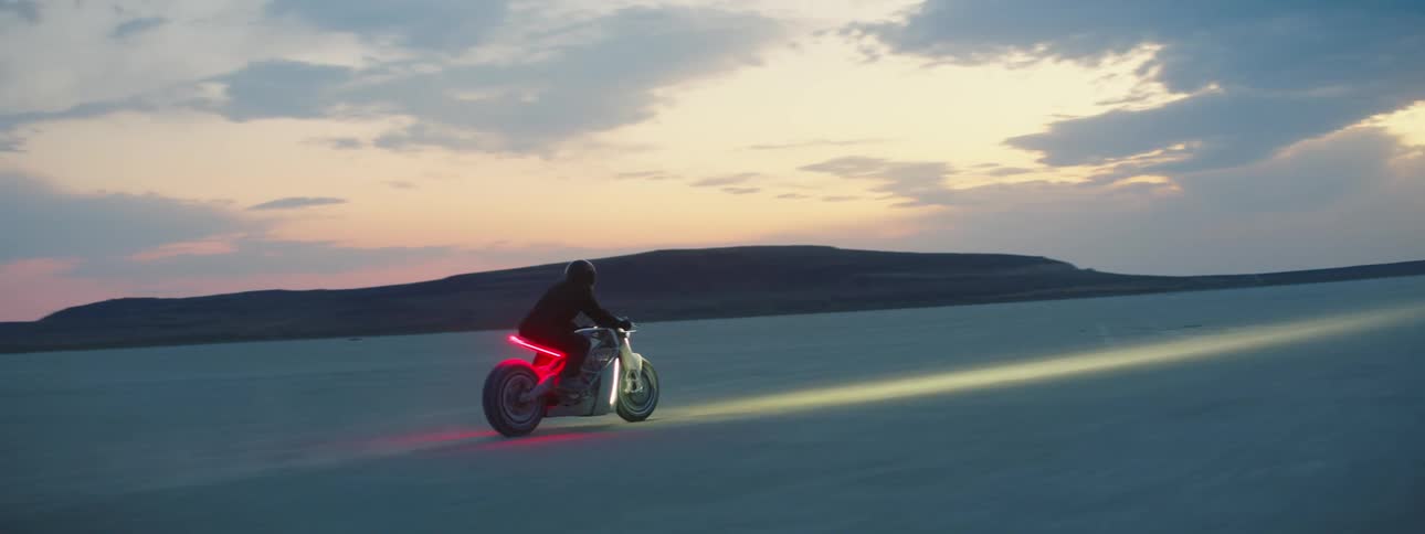 Motorcyclist rides across desert under red sky on motorcycle with red lighting