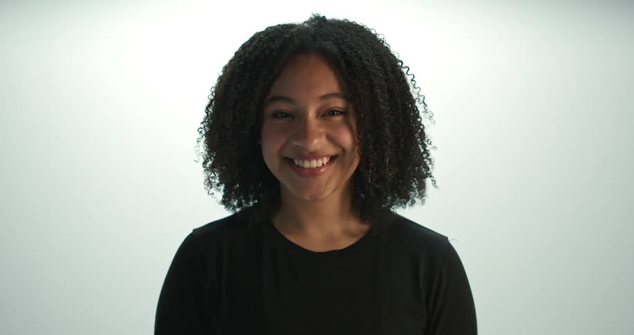 Woman pushes her hair back as she stands smiling against a bright background