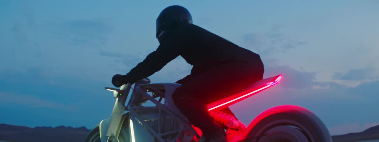 Motorcyclist rides across arid plain on motorcycle with rear lit by red lighting