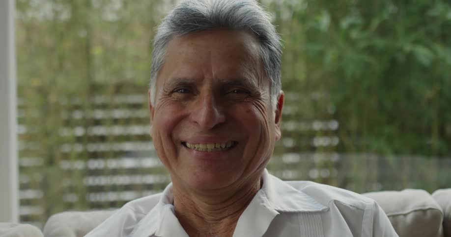 A man is sitting on his couch near a window with a smile on his face