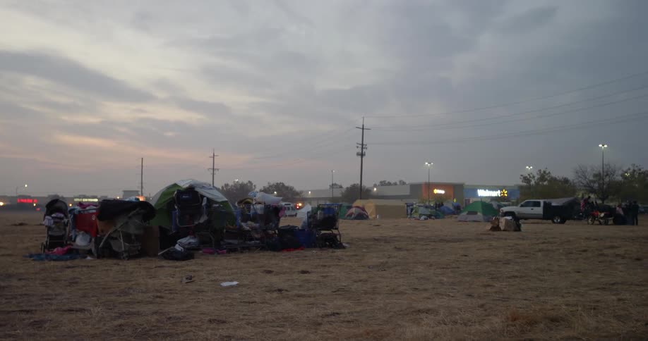 An open field contains tents for people who lost their homes in the Paradise fire disaster behind them the stores in a small strip mall