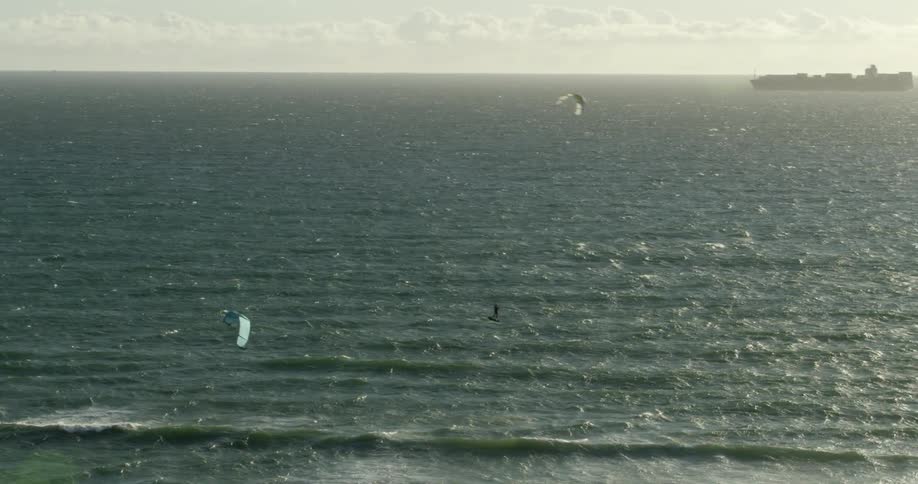 People kitesurfing on ocean waves with a ship in the distance