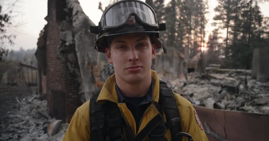 Fireman standing in front of a whats left of a building that burned down in a rural forest area