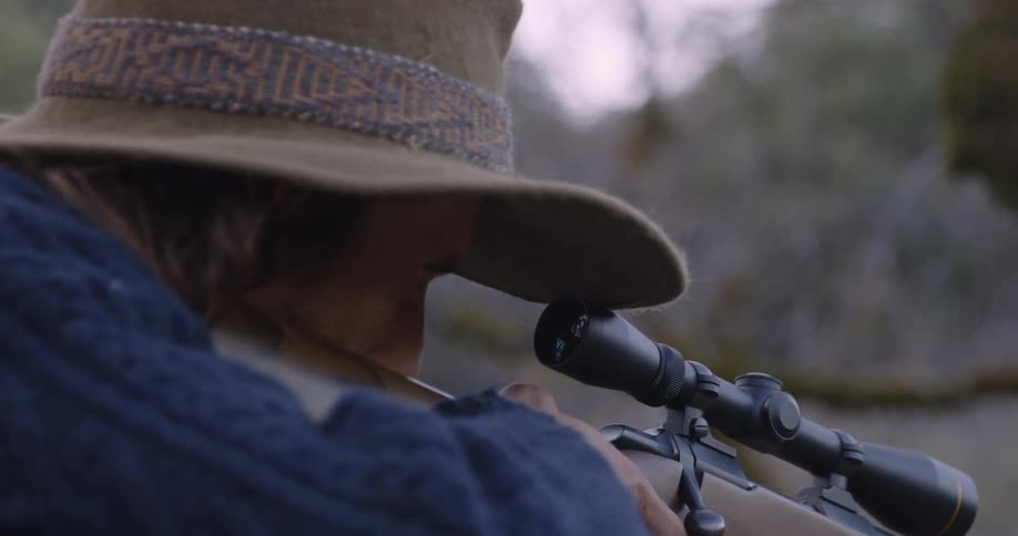 A man with a hat looks through the scope of his rifle